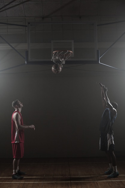 Dos jugadores de baloncesto en un gimnasio con uno anotando un lanzamiento