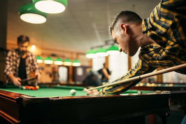 Dos jugadores de billar masculino con taco en la mesa