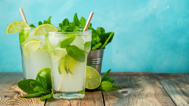 Dos limonadas caseras o cócteles de mojito con menta de lima y cubitos de hielo en un vaso en una mesa rústica de madera bebida fresca de verano con espacio para copiar