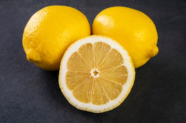 Dos limones enteros de Sicilia y la mitad en una piedra de pizarra oscura.