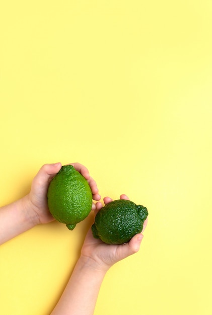 Dos limones lima en manos de los niños sobre un fondo amarillo