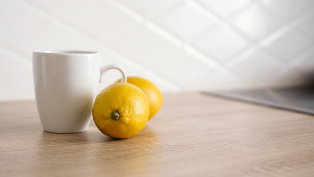 Dos limones en la mesa de la cocina cerca de una taza de té blanco. Concepto de mañana
