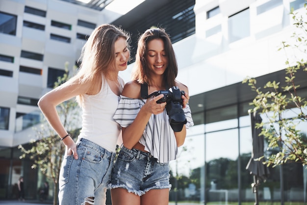 Dos lindas amigas de la chica con la cámara toman fotos juntas y caminan por la ciudad