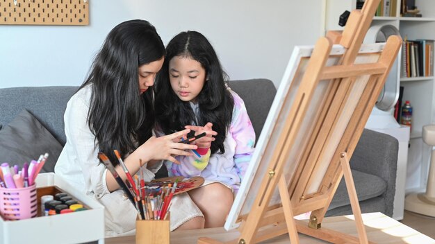 Dos lindas chicas asiáticas pintando cuadros en la sala de estar mientras pasan tiempo libre juntas