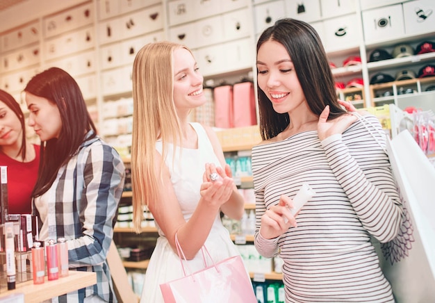 Dos lindas chicas en el frente están de pie y sonriendo. La muchacha asiática está mirando los cosméticos que la muchacha ciega tiene en la mano. Chica rubia está mirando a una chica asiática y sonriendo