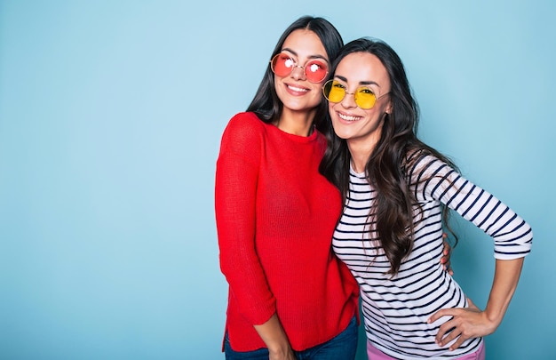 Dos lindas y encantadoras amigas con gafas de sol posando con una sonrisa en el fondo azul