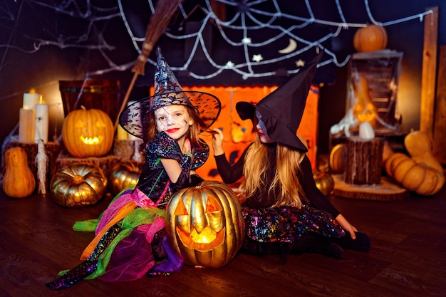 Dos lindas hermanas divertidas celebran la fiesta. Niños alegres en disfraces de carnaval listos para Halloween en decoraciones de Halloween