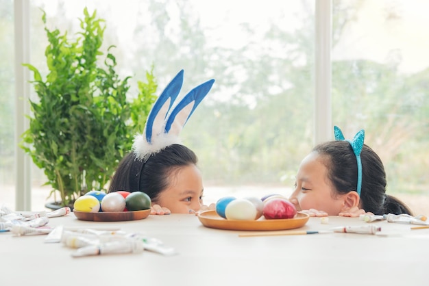 Dos lindas hermanitas con orejas de conejo jugando a la caza de huevos en Pascua adorables niños celebran la Pascua en casa Adolescente asiática pintando y decorando huevos de Pascua