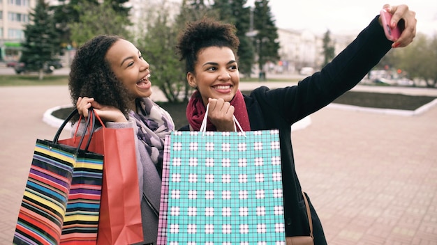 Dos lindas mujeres afroamericanas tomando selfie con bolsas de compras y sonriendo