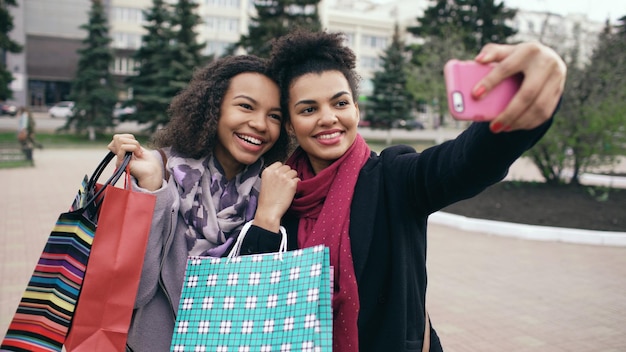 Dos lindas mujeres afroamericanas tomando selfie con bolsas de compras y sonriendo