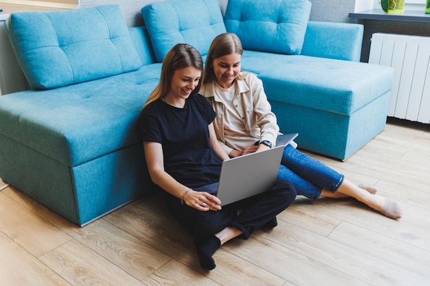 Dos lindas mujeres que trabajan usando una computadora portátil en la sala de estar en el sofá Amigos tiempo de amistad juntos Las novias están sentadas en el sofá y viendo una película