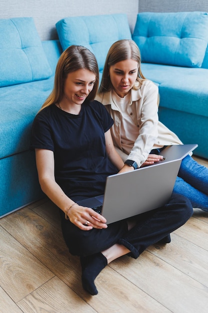 Dos lindas mujeres que trabajan usando una computadora portátil en la sala de estar en el sofá Amigos tiempo de amistad juntos Las novias están sentadas en el sofá y viendo una película