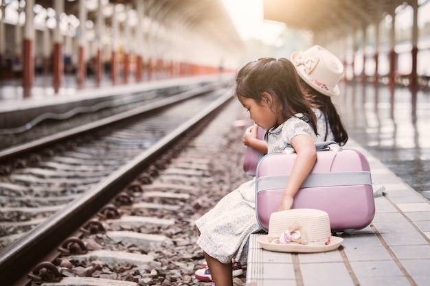 Dos lindas niñas asiáticas esperando el tren con maleta