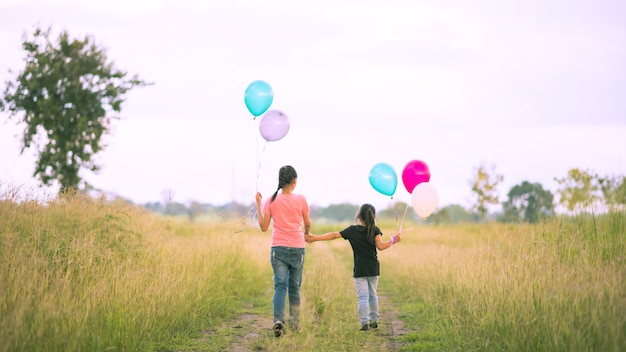 Dos lindas niñas corriendo en el prado verde con globos coloridos en la mano