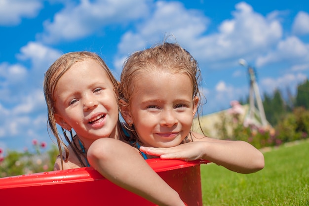 Dos lindas niñas felices divirtiéndose en una pequeña piscina en el patio al aire libre y disfrutan de las vacaciones