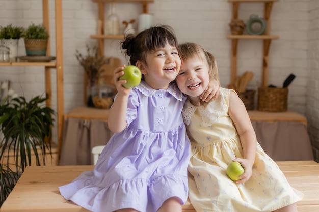dos lindas niñas graciosas vestidas comiendo manzanas verdes en la cocina. espacio para texto, pancarta