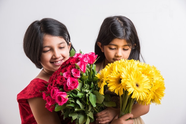 Dos lindas niñas indias sosteniendo un ramo de rosas rojas frescas o flores Gulab. Aislado sobre fondo blanco