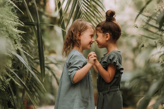 Dos lindas niñas sonrientes en ropa de lino cogidos de la mano y caminando en el jardín botánico