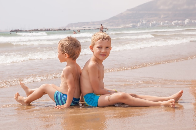 Dos lindos adorables hermanitos muchachos sentados en la playa mar océano