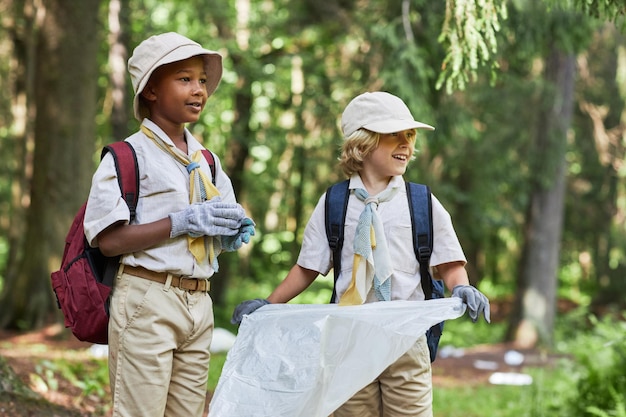 Dos lindos boy scouts ayudando a limpiar el bosque y sosteniendo una bolsa de basura