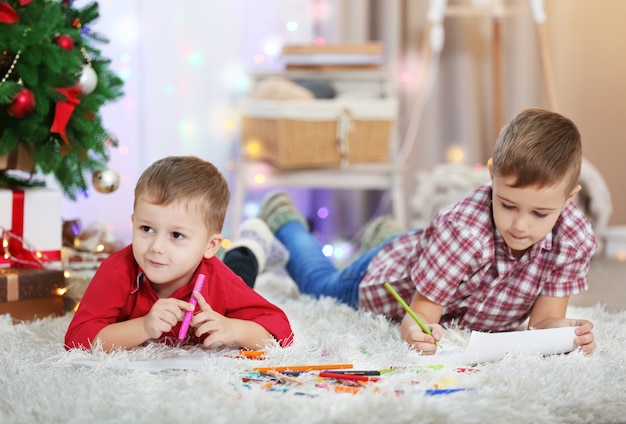 Dos lindos hermanos pequeños dibujando sobre fondo de árbol de Navidad
