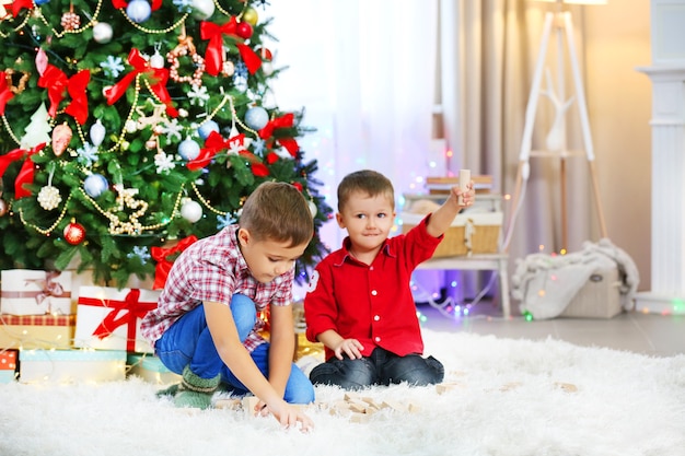 Dos lindos hermanos pequeños jugando con juguetes de madera en la superficie del árbol de Navidad