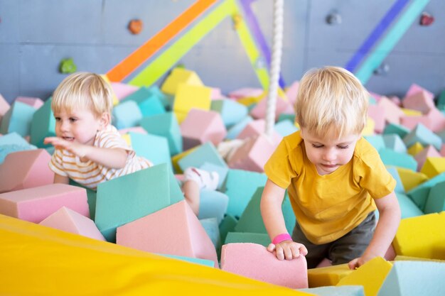 Dos lindos niños gemelos juegan con cubos suaves en la piscina seca en el centro de juegos