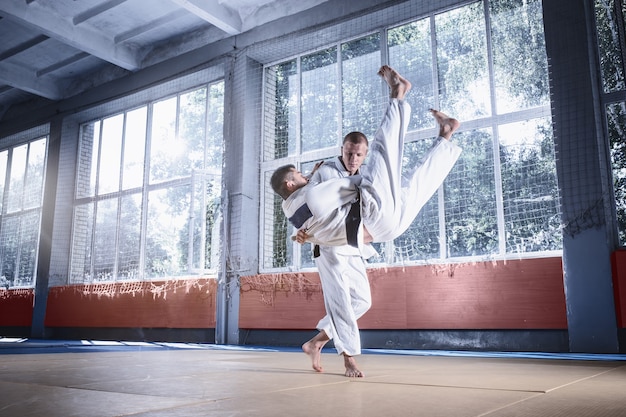 Dos luchadores de judo que muestran habilidad técnica mientras practican artes marciales en un club de lucha. Los dos hombres de uniforme. lucha, kárate, formación, artes, atleta, concepto de competencia