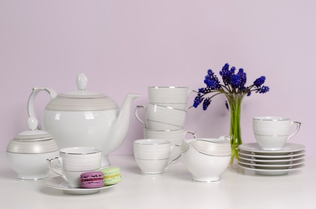 Dos macarrones y un juego de té y café de porcelana o vajilla con flores azules en la mesa blanca.