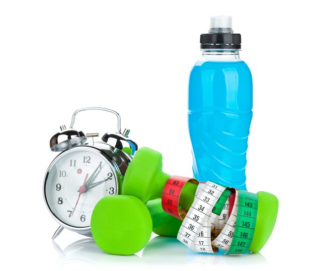 Dos mancuernas verdes, cinta métrica, botella de bebida y despertador. Condición física y salud. Aislado sobre fondo blanco