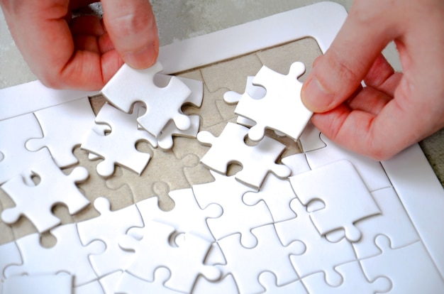 Dos mano sosteniendo una pieza de puzzle incompleto rompecabezas blanco sobre la mesa