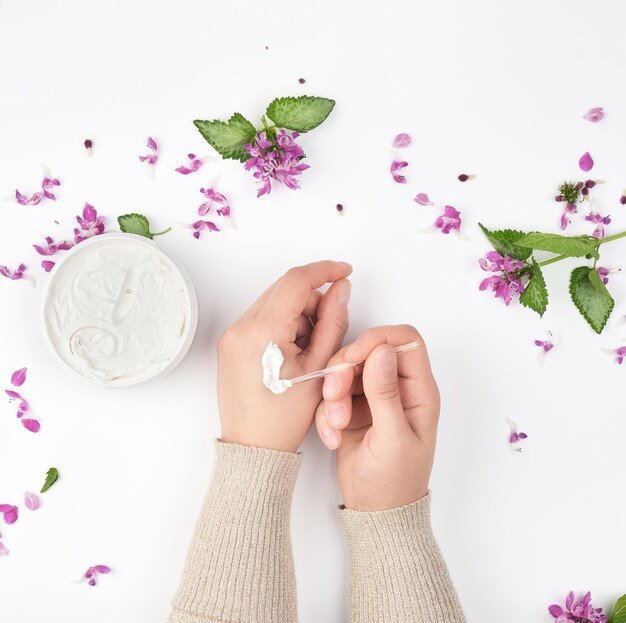 Foto dos manos femeninas y un frasco con crema espesa y flores rosas