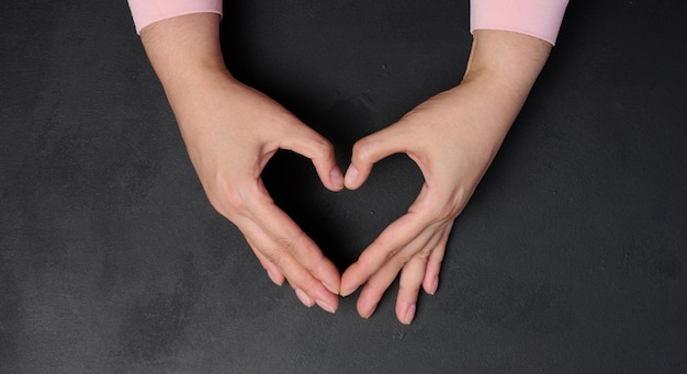 Foto dos manos femeninas plegadas en forma de corazón sobre un fondo negro