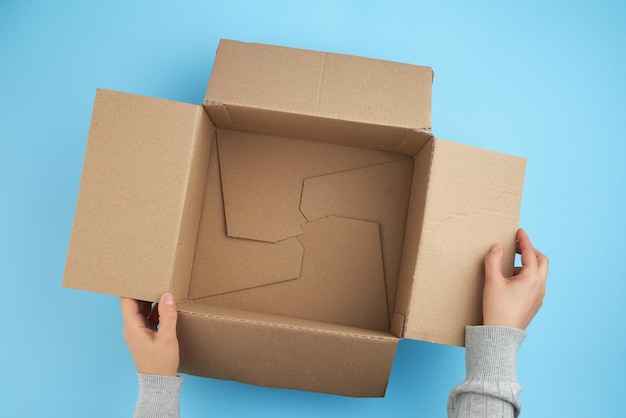 dos manos femeninas sosteniendo una caja vacía abierta de cartón marrón en la parte inferior hay una espuma blanca para el embalaje vista superior concepto de embalaje de cosas