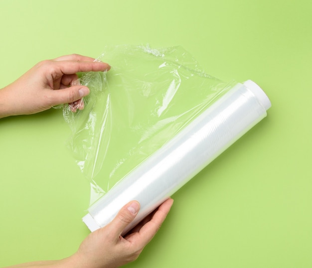 Dos manos femeninas sostienen un rollo de film transparente para envasar productos, fondo verde