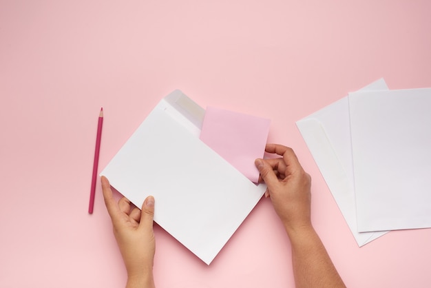 Dos manos femeninas sostienen un sobre de papel blanco sobre una superficie rosa