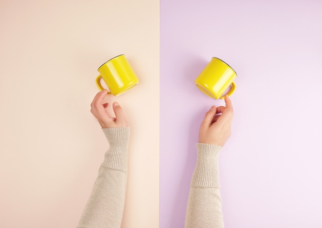 Dos manos femeninas sostienen tazas de cerámica amarillas.