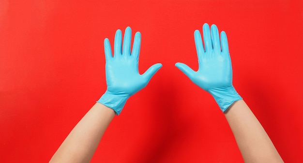 Dos manos con guantes de látex azul o guantes quirúrgicos sobre un fondo rojo. Mano vacía.