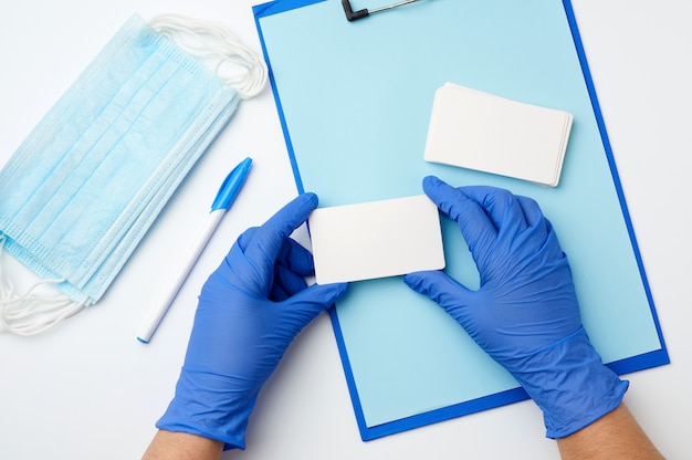 Dos manos en guantes médicos azules sostienen tarjetas de visita rectangulares en blanco