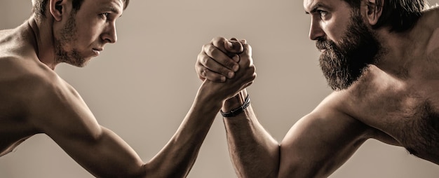 Foto dos manos de hombres entrelazadas lucha de brazos, fuertes y débiles, pareja desigual. hombre barbudo muy musculoso que lucha con un hombre débil enclenque.