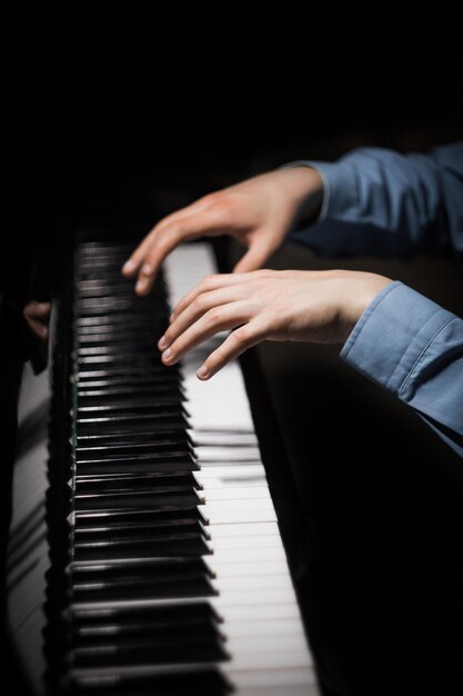 Dos manos masculinas en las palmas del piano yacen sobre las teclas y tocan el instrumento del teclado en la escuela de música. El estudiante aprende a tocar las manos. El pianista negro fondo oscuro vertical.