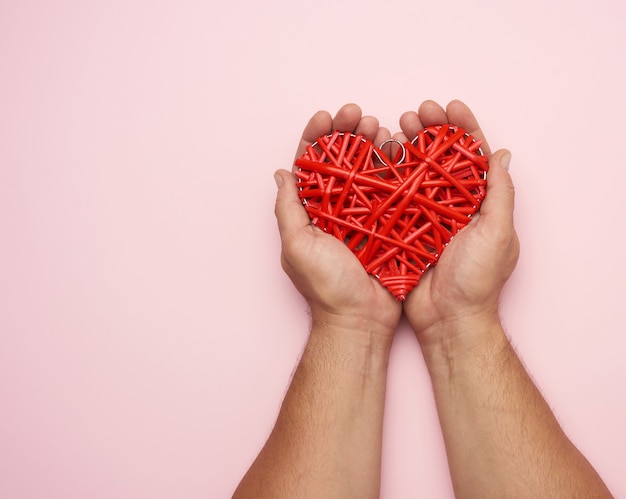 Dos manos masculinas sosteniendo un corazón de mimbre rojo sobre un rosa