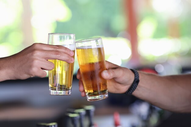 Dos manos masculinas sostienen un vaso de cerveza fría y tintinean vasos.