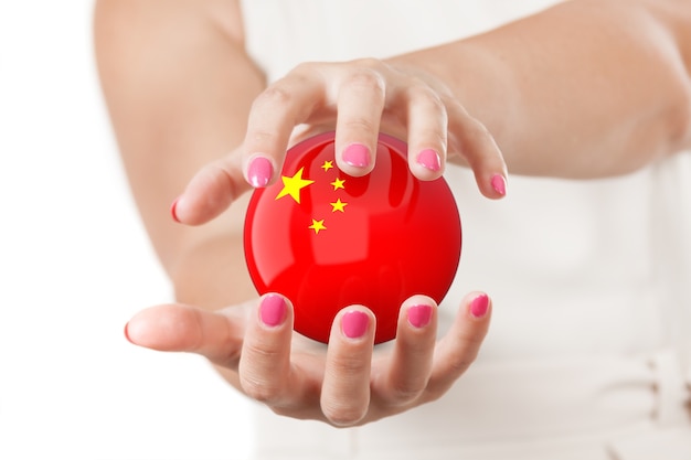 Dos manos de mujer que protegen la esfera del globo terráqueo de la bandera de China sobre un fondo blanco.
