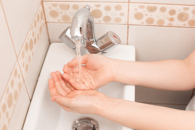 Dos manos de niños sobre el lavabo en el baño con agua vertida