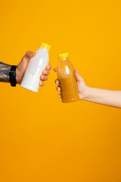 Dos manos sosteniendo botellas con bebidas en el estudio sobre un fondo amarillo