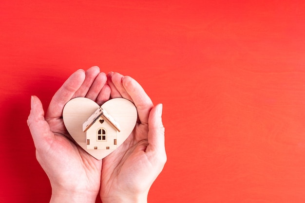 Dos manos sostienen una forma de corazón de madera y una casa de madera, símbolo de la familia, el amor, las relaciones