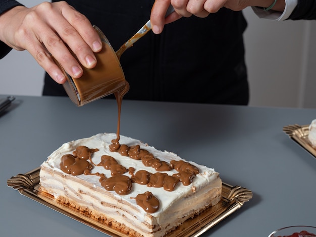 Dos manos vertiendo líquido marrón sobre pastel blanco de un vaso transparente