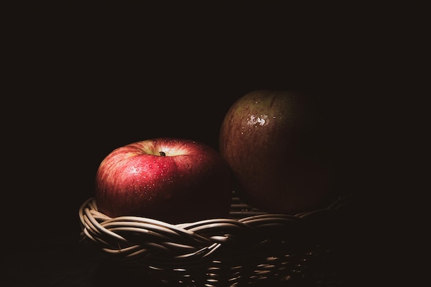 Dos manzanas rojas frescas en una canasta Sobre un fondo negro con luces de gotas de agua están cayendo con espacio para texto