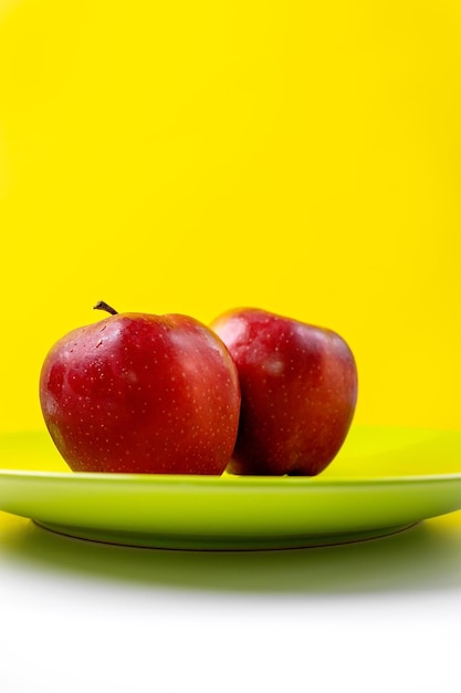 Dos manzanas rojas en un plato verde con un fondo amarillo
